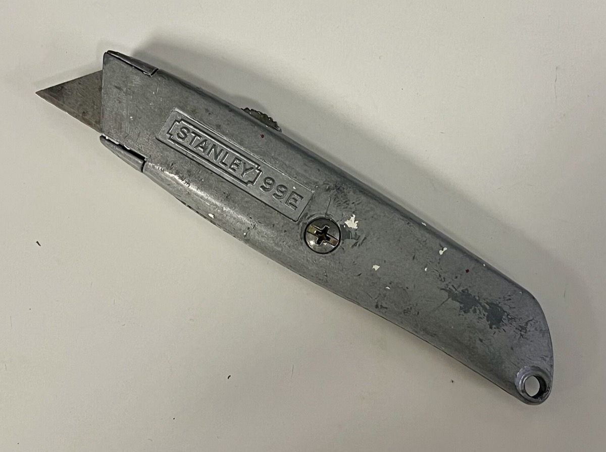 A worn, silver Stanley 99E retractable utility knife with the blade extended, on a white surface